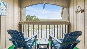 A covered outdoor seating area with two Adirondack chairs, a small table, and a view through a window.