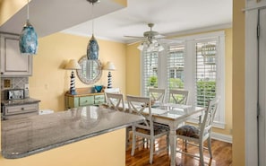 A kitchen with a dining table, chairs, a ceiling fan, and a window with blinds.