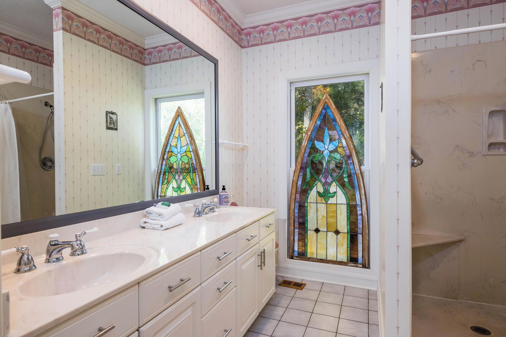 A bathroom with a large mirror, two sinks, a shower, and a stained glass window.