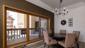 Ein Essbereich mit einem großen Schiebeglastür, die auf einen Balkon führt, einer Kristallleuchtre und einem Wanddekor im Sonnenstrahl-Design.