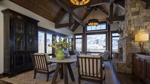 A rustic interior with wooden beams, a stone fireplace, and a view of mountains through large windows. - 23 Powder Ridge - Managed by Purgatory Resort (Durango)