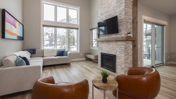 A modern living room with a stone fireplace, large windows, and a flat-screen TV. - 103 Travertine Trail - New Build - Managed by Purgatory Resort (Durango)