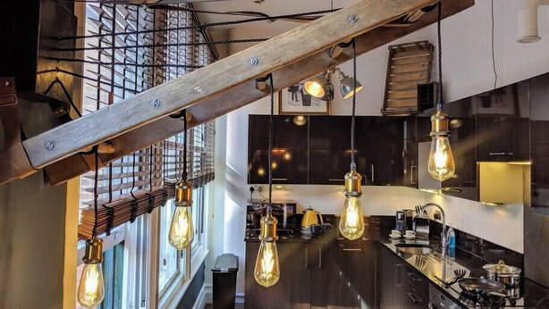 Una cocina moderna con estructura de vigas de madera, iluminación colgante y vista al área de estar.