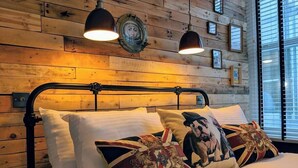 Una cama con estructura metálica, ropa de cama blanca y almohadas con diseños de la bandera del Reino Unido.