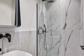 A modern bathroom with a marble shower wall, a handheld showerhead, and a wall-mounted faucet.
