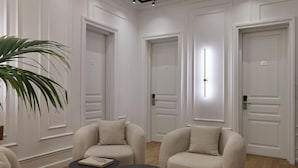 A modern hotel room with a minimalist design, featuring three beige armchairs, a small round table, and a large potted plant.