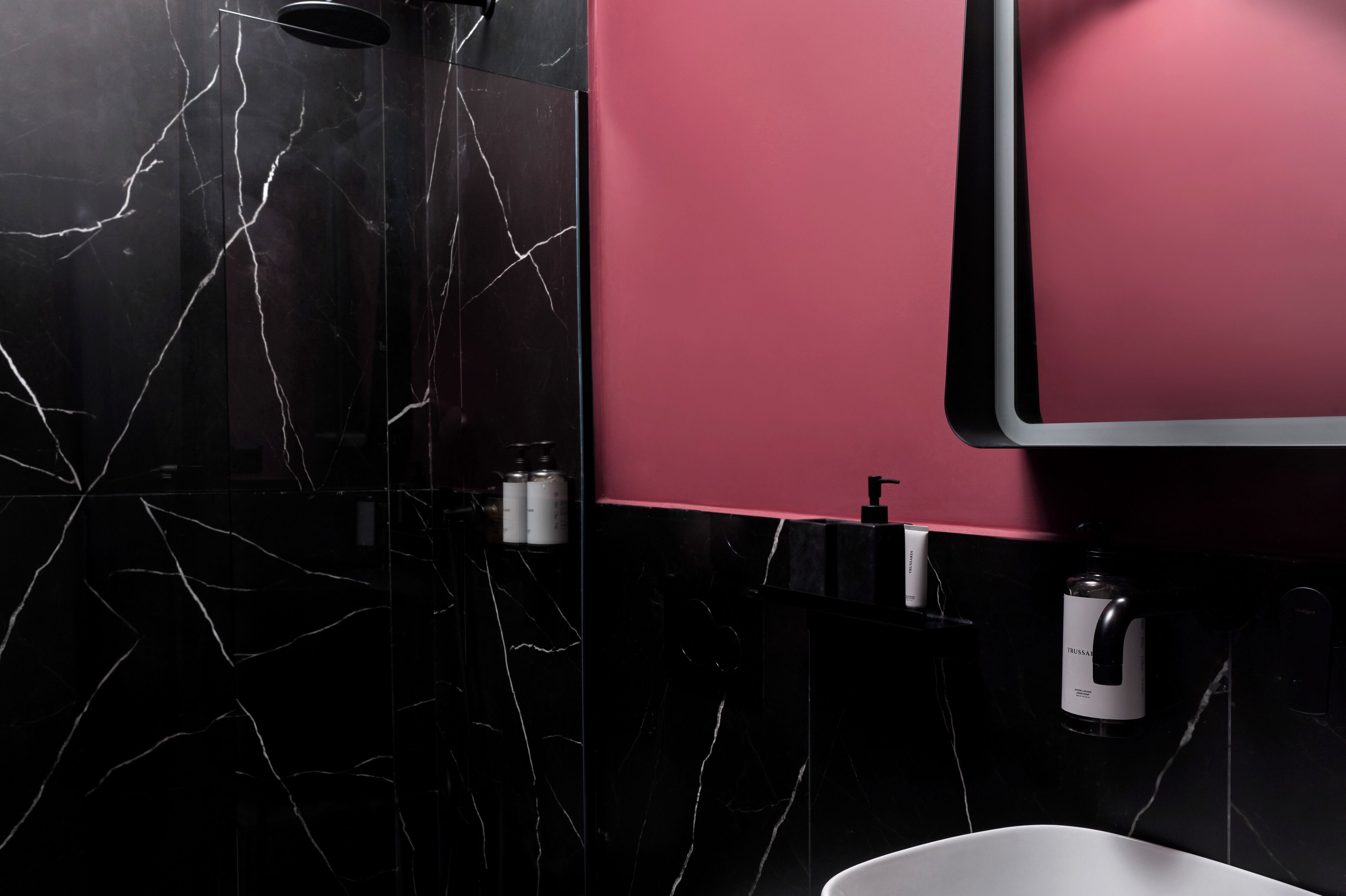 A bathroom with a black marble wall, a pink accent wall, and a white sink.