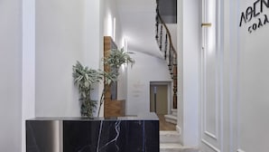 A modern reception area with a marble counter, potted plants, and a staircase leading to the upper floor.