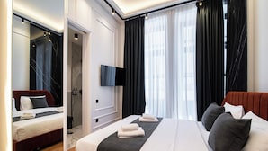 A modern hotel room with a large bed, a smaller bed, a TV, and a bathroom with a mirror and curtains.
