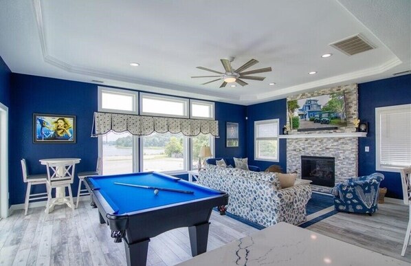A room with a pool table, a fireplace, and a view of the outdoors.