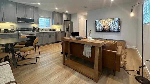A modern kitchen with built-in appliances, a dining area with a wooden table and chairs, and a living area with a sofa and a painting on the wall. - Stay in Style & Elegance (Burbank)