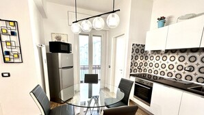 A modern kitchen with a glass dining table, black chairs, a stainless steel refrigerator, and a patterned backsplash.