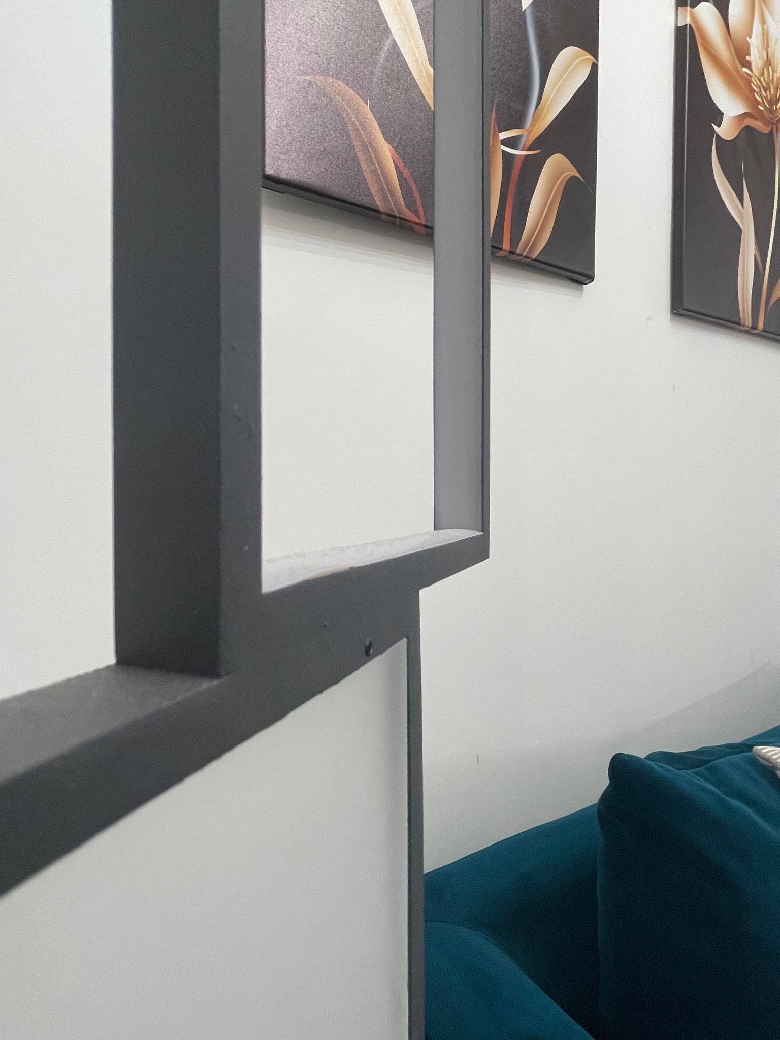 En modern inredning med ett geometriskt mönster på väggen, en turkosfärgad soffa och abstrakt blomstermotiv i form av konstverk.