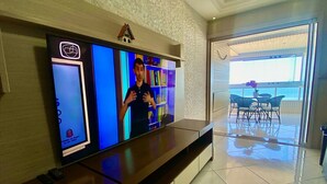 A reception area with a large flat-screen TV, a small house decoration, and a view of an outdoor patio with chairs. - Residencial Las Brisas (Praia Grande)