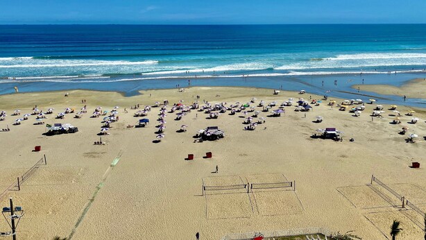 A beach with umbrellas, sun loungers, and a volleyball court. - Residencial Las Brisas (Praia Grande)