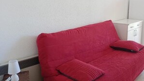 Ein rotes Sofa mit passender Kissen in einem Raum mit weißen Wänden und einem weißen Schrank.