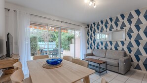 A modern living room with a dining area, a grey sofa, and a patterned wall. - Renovated 2-Bed Apt in Biscarrosse Plage, Sleeps 4, Ocean View Terrace, Pet-Friendly (Biscarrosse Plage)