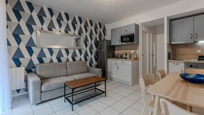 A compact living space with a sofa, coffee table, dining table, and chairs. A kitchenette is visible with a microwave, stove, and cabinets. - Renovated 2-Bed Apt in Biscarrosse Plage, Sleeps 4, Ocean View Terrace, Pet-Friendly (Biscarrosse Plage)