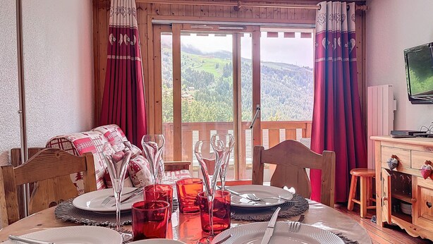 A dining area with a table set for four, a wooden chair, a television, and a scenic view through the window.