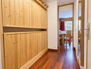 A room with wooden paneling, a dining area with chairs and a table, and a view through an open doorway.