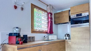 A compact kitchen with wooden cabinets, a built-in oven, and a window with a curtain.