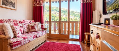 A cozy room with a wooden sofa, a red rug, a wooden cabinet, and a large window with curtains.