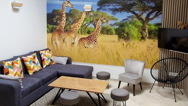 A living room with a sofa, coffee table, and chairs, a TV mounted on the wall, and a mural of giraffes. - Spacious house, private pool - 11 guests (La Flèche)