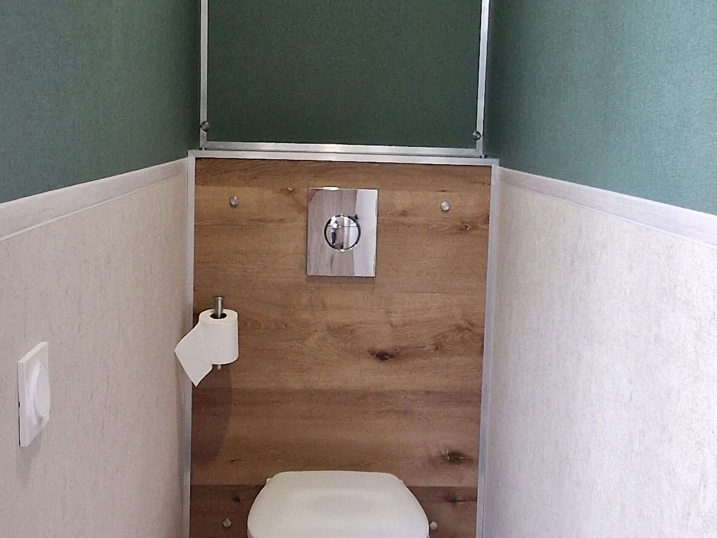 Een kleine, smalle badkamer met een houten paneelwand, een toilet en een papieren handdoekhouder.