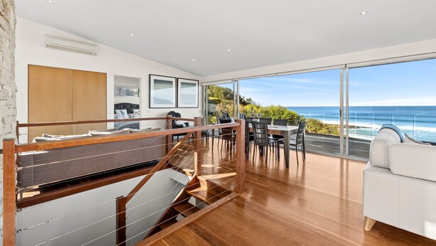 Un interior moderno con una escalera de madera, una zona de comedor con vista al océano y un sofá blanco.