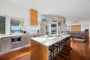 A modern kitchen with a central island, large windows, and a stone accent wall. - Sandbanks (Separation Creek)