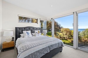 A bedroom with a large bed, two bedside lamps, a nightstand, and a view of the outdoors. - Sandbanks (Separation Creek)