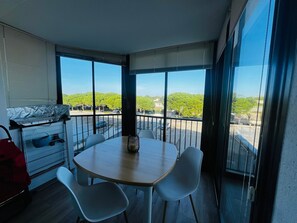 A balcony with a view of a parking lot and greenery, a round table with chairs, and a kitchen area with a stove and a basket. - 2-Bedroom Apartment in Argelès-sur-Mer with Parking and Air Conditioning (Argelès-sur-Mer)
