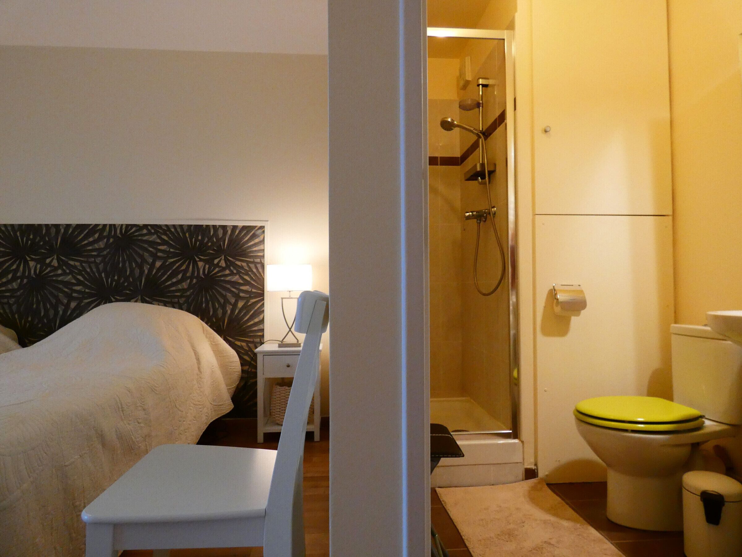 A hotel room with a bed, a bedside table with a lamp, a shower area, and a toilet.