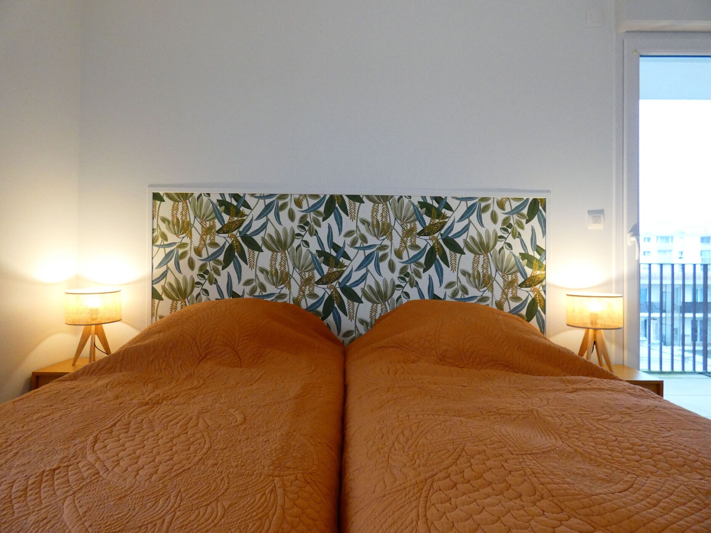 A hotel room with a large bed, two bedside lamps, and a patterned headboard.