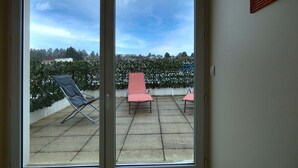Una habitación con puerta de vidrio corrediza que da a un patio exterior con dos sillones y una pequeña mesa.