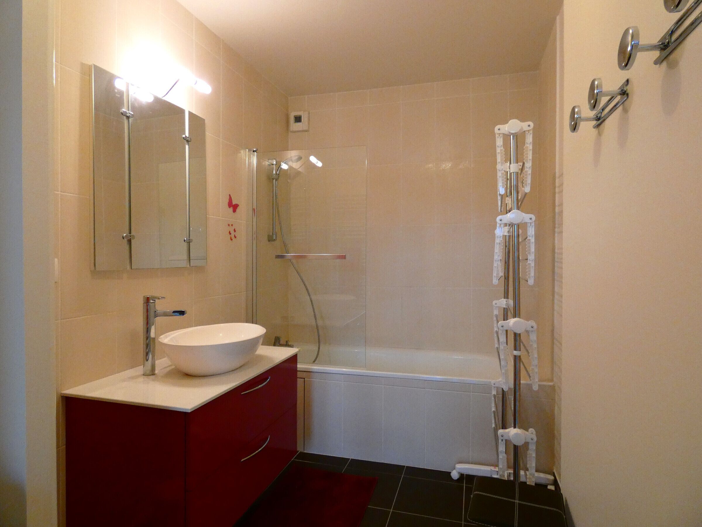 Ein modernes Badezimmer mit weißem Waschbecken, rotem Schminktisch und einer begehbaren Dusche mit Glastür.