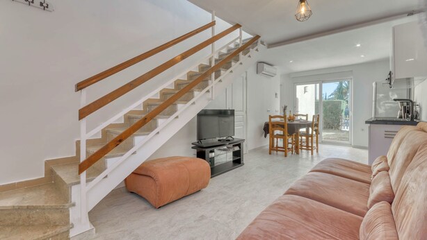 A modern living room with a staircase, a flat-screen TV, a dining area with a table and chairs, and a kitchen area. - Superbe Maison de Vacances à Santa Margarita Immo365 (Roses)