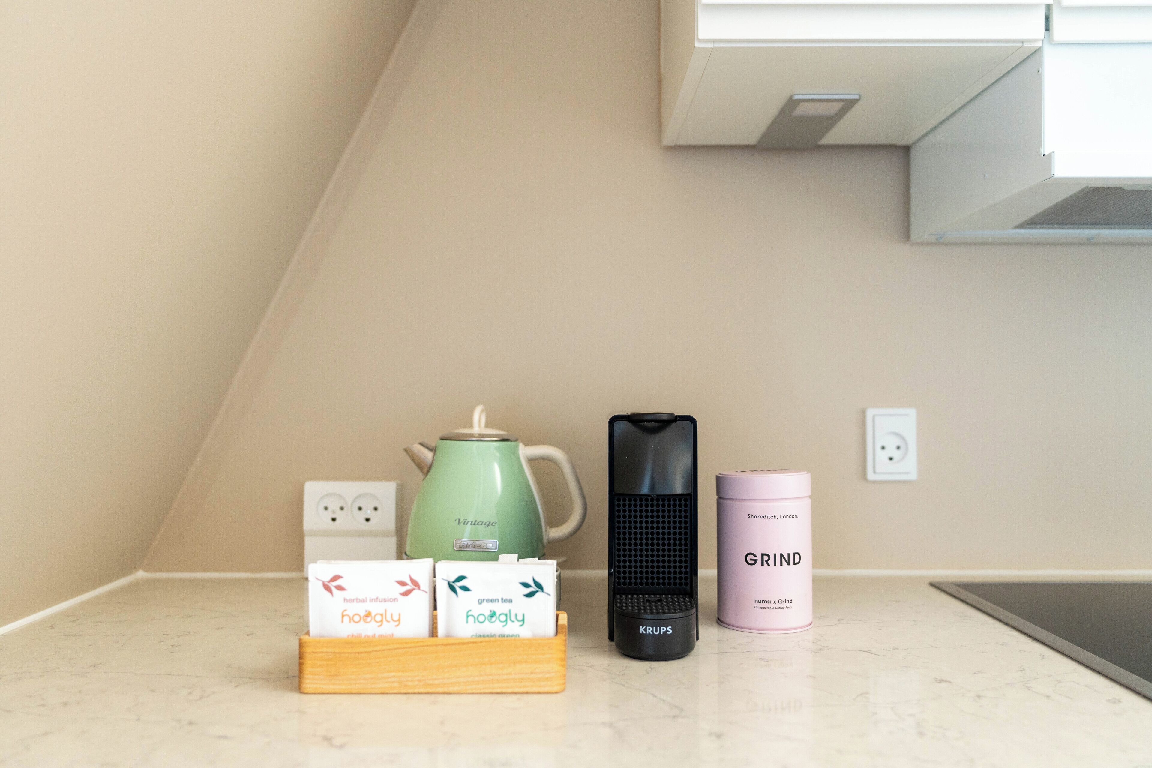 A kitchen counter with a kettle, a coffee maker, and a container labeled "GRIND".