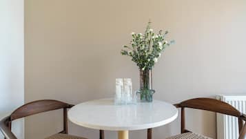 Et rundt bord med to fletstole, en vase med hvide blomster og to vandflasker.