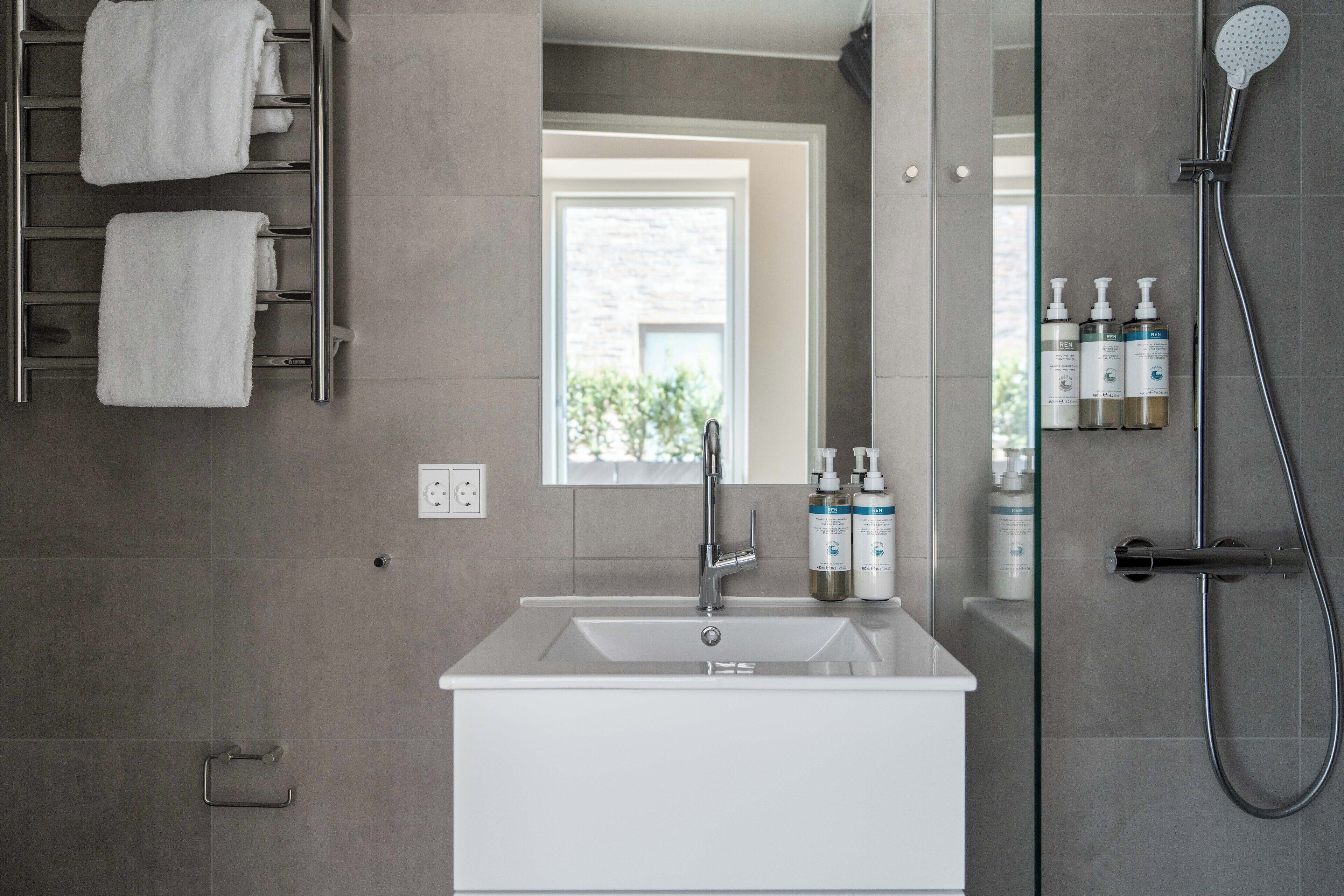 Un baño moderno con un lavamanos blanco, una cabina de ducha de vidrio y un perchero con dos toallas.