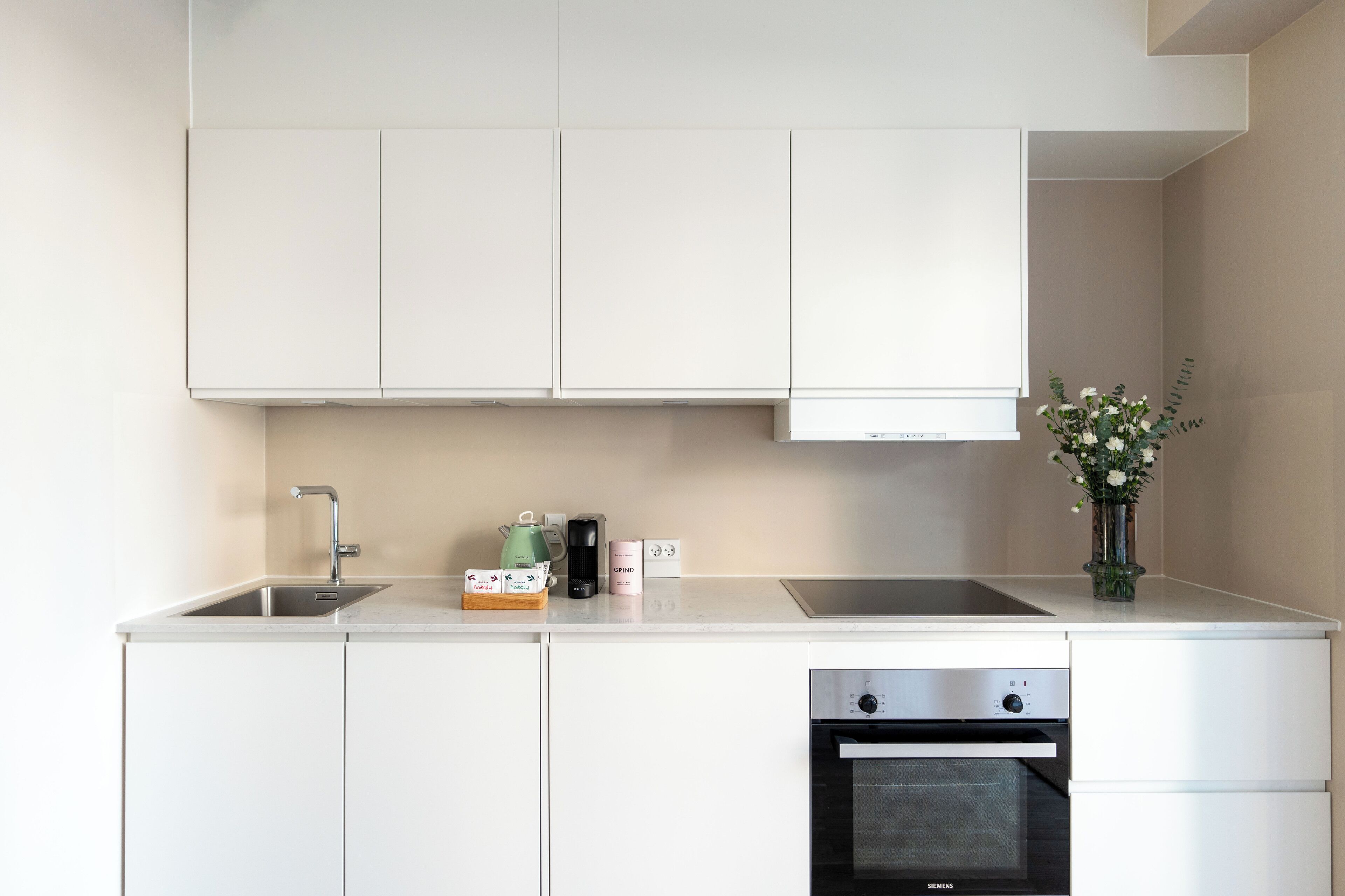 Een moderne keuken met witte kastjes, een roestvrijstalen spoelbak, een koffieapparaat, een broodrooster en een inbouwoven.