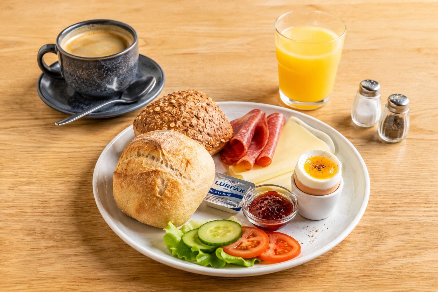 A breakfast plate with bread, cheese, ham, egg, and vegetables, a cup of coffee, and a glass of orange juice on a wooden table.