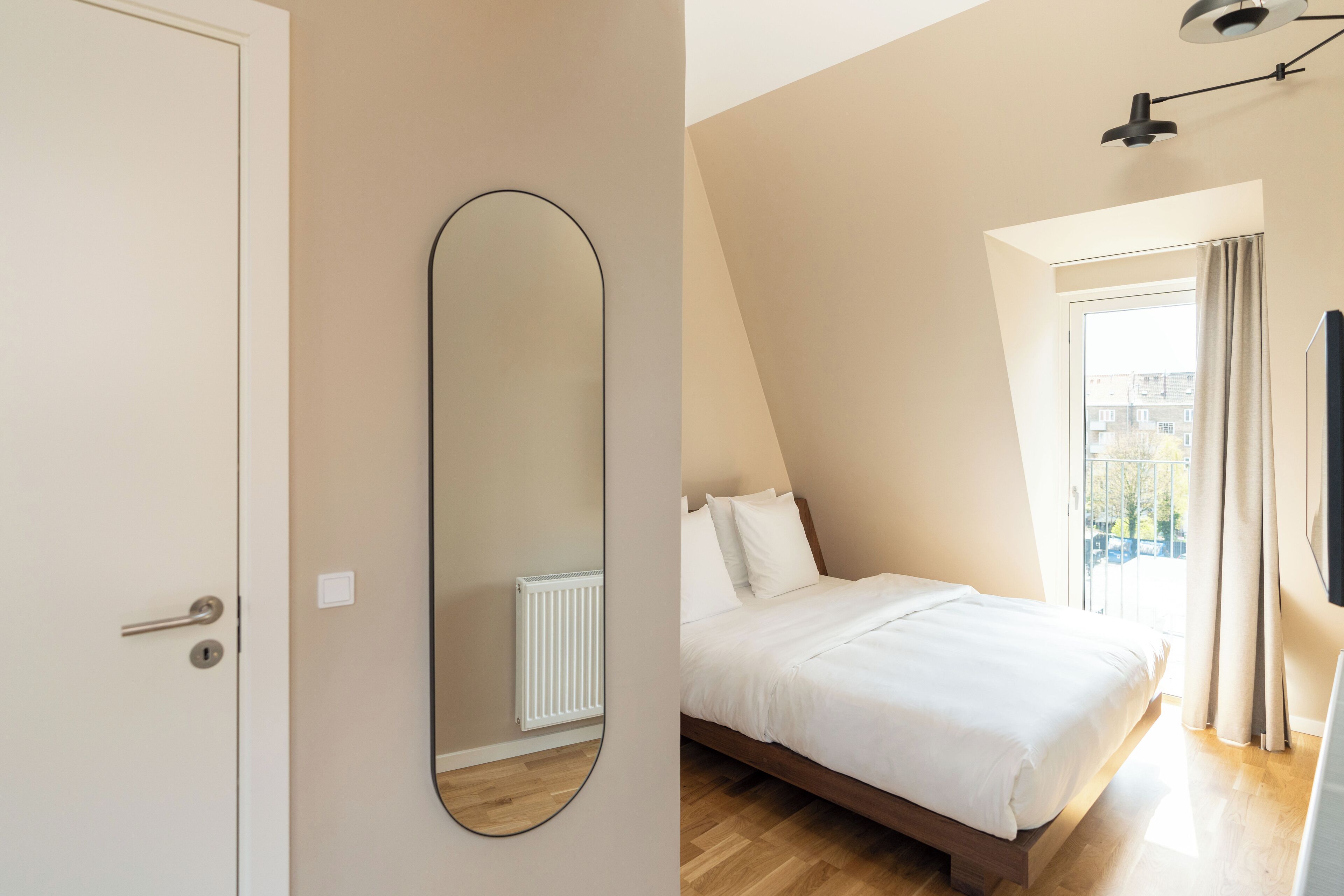 A bedroom with a bed, a large mirror, a radiator, and a window with curtains.