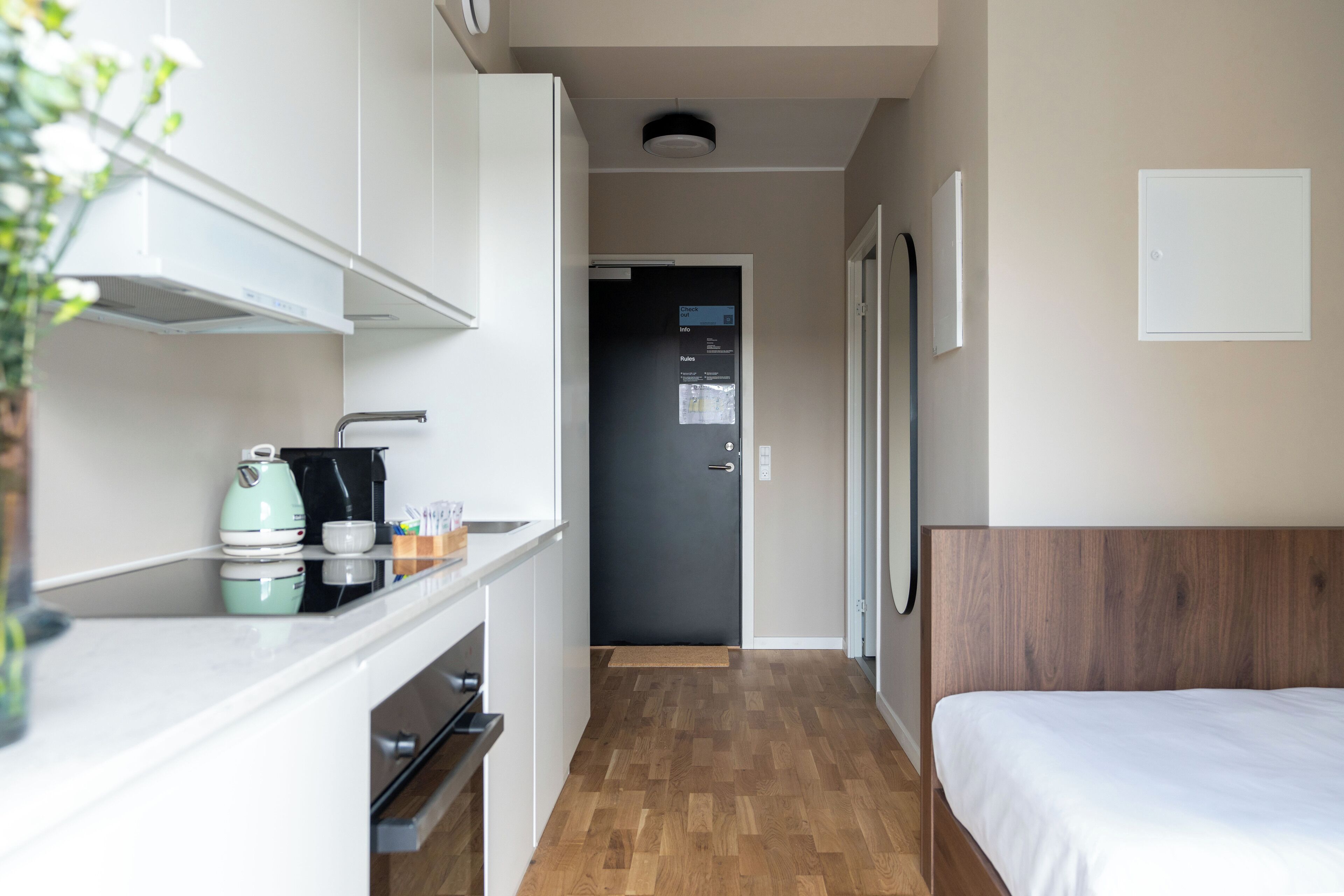 Una habitación de hotel compacta con kitchenette, una cama y una puerta que da a un pasillo.