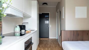 Una habitación de hotel compacta con kitchenette, una cama y una puerta que da a un pasillo.