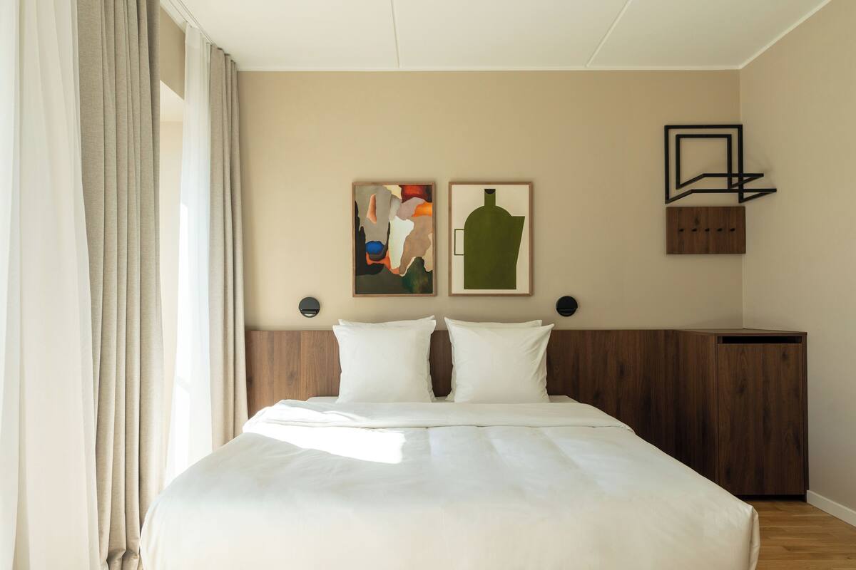 Habitación de hotel con una cama grande, dos obras de arte colgadas en la pared, cabecero de madera y un armario empotrado.