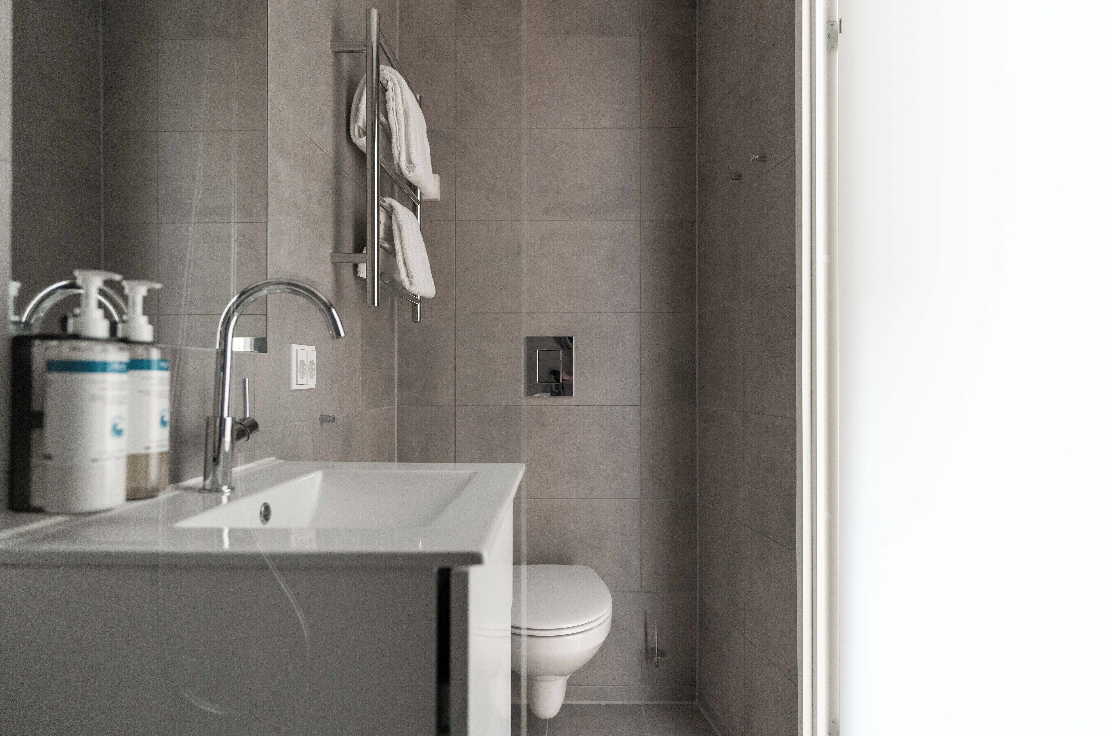 A modern bathroom with a white sink, a shower, and a toilet.