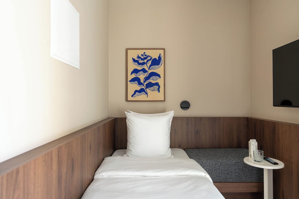 Habitación de hotel con una cama, una mesita con un control remoto, una botella y una obra de arte enmarcada en la pared.
