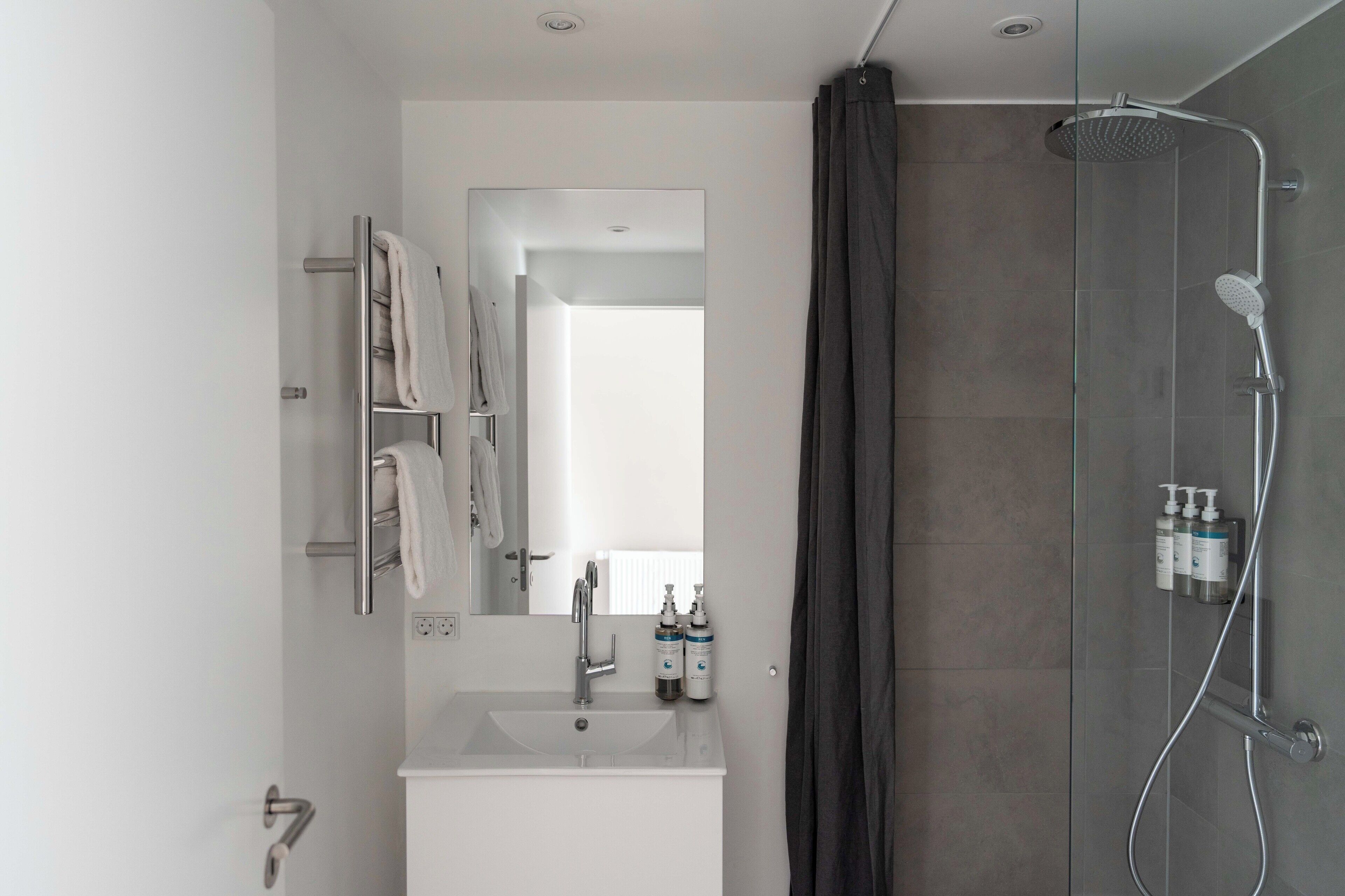 Ein modernes Badezimmer mit Duschkabine aus Glas, Waschbecken in Weiß und Spiegel mit Handtuchhalter.