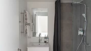 Ein modernes Badezimmer mit Duschkabine aus Glas, Waschbecken in Weiß und Spiegel mit Handtuchhalter.